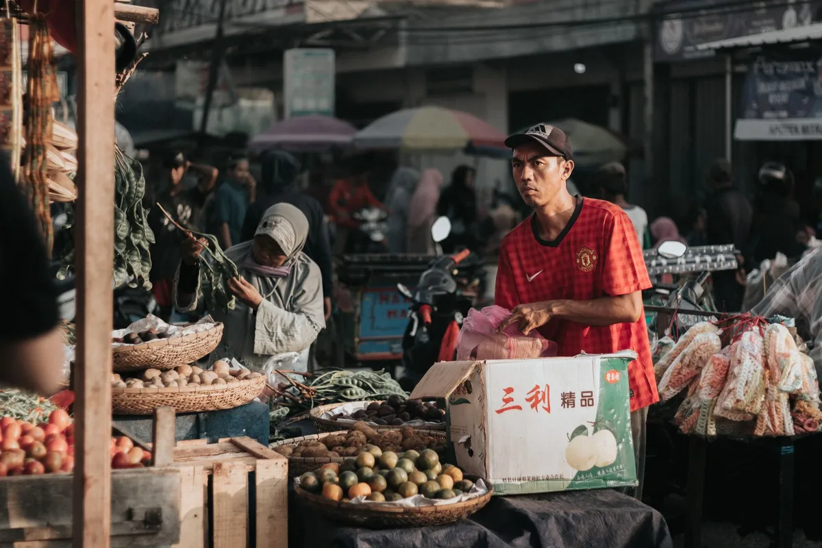 Penjual di pasar Indonesia mengelola produk dagangannya, seperti halnya penjual online di Tokopedia mengelola pesanan