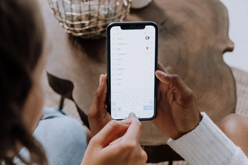 Tangan memegang smartphone menampilkan antarmuka aplikasi belanja online, seperti halaman utama Shopee Indonesia