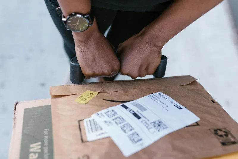 Seller carefully packing an order in a white box with bubble wrap, shipping label printed and ready for courier pickup