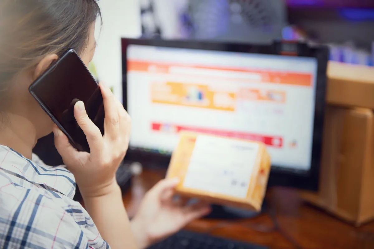 Filipino seller reviewing Shopee marketplace orders on a smartphone with packaged products and poly mailers on the desk