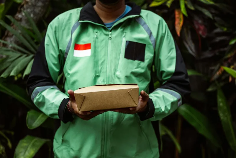 Delivery courier in green jacket holding a parcel box for marketplace order fulfillment and last-mile delivery